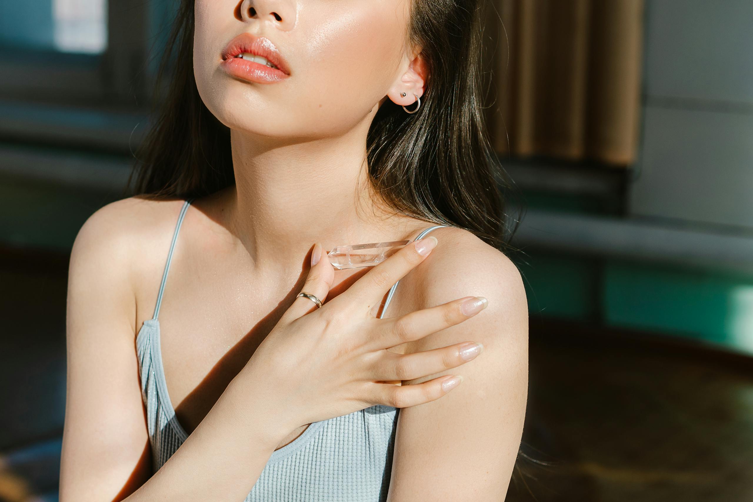 Close-up of a woman in soft lighting wearing a tank top, showcasing elegance and natural beauty.